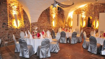 Gewölbter Natursteinkeller festlich eingerichtet für Hochzeit mit silbernen Stuhlhussen